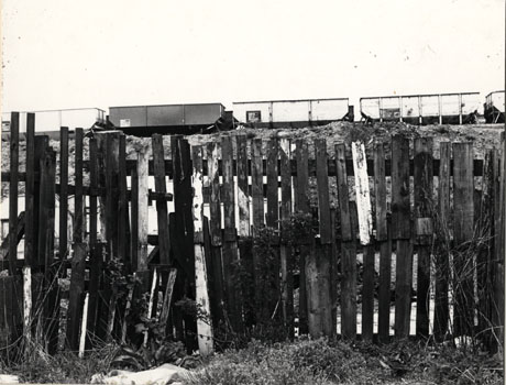 Photograph of five coal trucks on an embankment, with the fence of, possibly, an allotment in the foreground at Horden