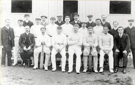 Photograph of the eleven players and eleven other men, members of Horden Cricket Club, posed in front of a wooden building; the players are dressed in cricket whites and tow are holding bats