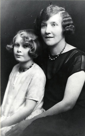 Photograph of the head and torso of a woman and a girl of approximately eight years of age; the woman has waved hair and is wearing a dark dress and a necklace; the girl has a loose light coloured dress and a necklace and short hair; they have been identified as Mrs. Turnbull and daughter, Winnie, from Horden
