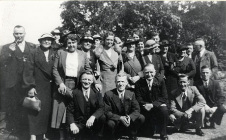 Photograph of a group of fifteen middle-aged women and nine middle-aged men posed in front of trees; all the people in the photograph are wearing formal clothes; the occasion on which the photograph was taken has not been identified