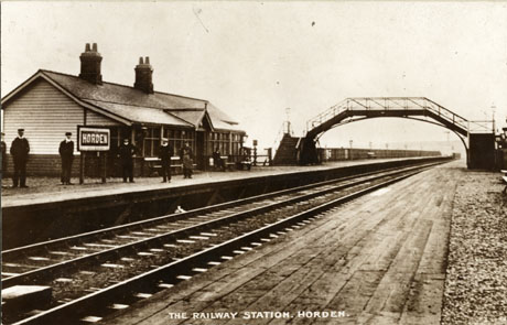 Postcard photograph entitled The Railway Station. Horden., showing the track leading away from the camera from left to right; one platform can be seen with the sign for Horden and the station buildings; seven indistinct figures can be seen on the platform; a footbridge over the track can be see in the middle distance; the photograph has been identified as looking South