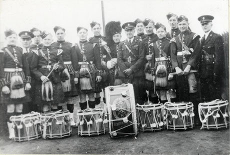 Photograph of twelve young men dressed in the uniform of Scottish soldiers, posed with three men in a military uniform; in front of the group are seven drums on the largest of which are the words Church Lads' Brigade Horden