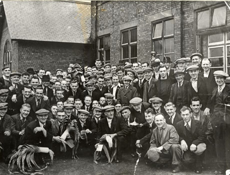 Photograph of a group of approximately one hundred men posed outside the Horden Workmen's Social Club; men on the front row are holding prize leeks and certificates; a man at the back on the right of the picture is holding up a trophy cup; all the men are dressed formally in suits, ties and caps
