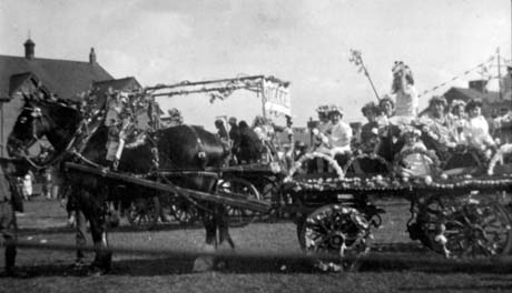 Photograph showing a horse pulling a cart, decorated with flowers along its wheels and along the edge of the cart; the harness of the horse is also decorated with flowers and there is a frame of flowers across his back; there are eight girls, aged between approximately five and thirteen years, dressed in light-coloured frocks and crowns on the cart; the photograph has been identified as Carnival, Horden