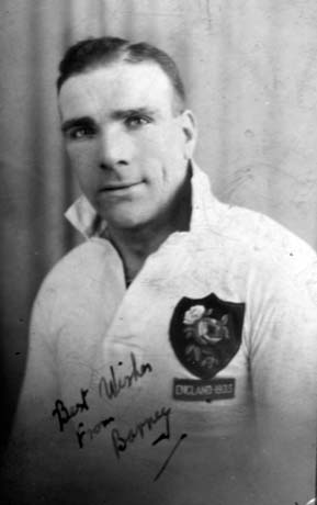 Photograph of the head and torso of a man wearing a shirt on which there is a shield with a rose and the words England 1935; the words Best Wishes From Barney are written on the photograph; he has been identified as Barney Hudson of Horden