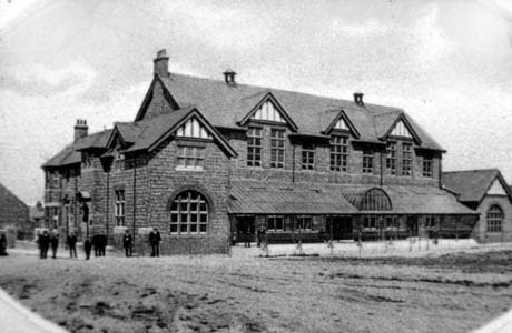 Photograph showing the exterior of a large building with three large windows on the first floor and a veranda on the ground floor; two wings are on either end of the building; twelve indistinct figures can be seen in front and at the side of the building; it has been identified as Horden Club and Institute, Horden