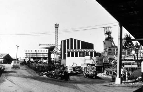 Photograph showing a road running to the left and a road running into the buildings of a colliery; a motor van is driving away from the camera up the road to the left; the centre of the photograph shows low buildings and the winding gear of the colliery are at the right of the picture; the colliery has been identified as Horden Colliery