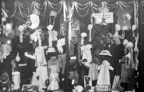 Photograph of the window of a draper's shop showing the garments on display, most of which appear to be children's clothes; one sign reads Xmas Presents and another A Merry Xmas; the photograph has been identified as Inside Kilburns' Shop, Horden