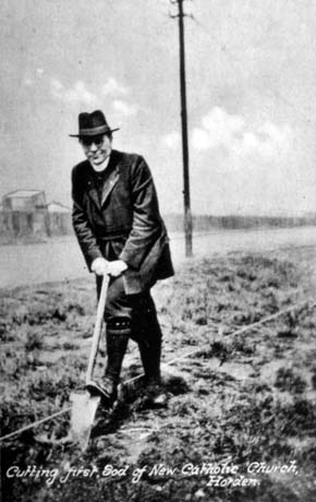 Postcard photograph, entitled Cutting First Sod of New Catholic Church, Horden, showing a clergyman wearing a trilby hat, dog collar, long jacket, breeches and gaiters, standing on a spot marked by a line of string, putting a spade into the ground; behind him is a road and indistinct buildings on its far side; he has been identified as Father Watson
