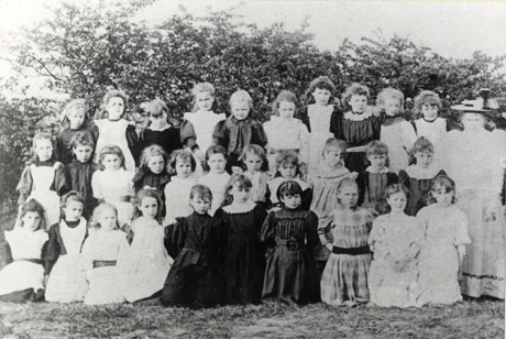 Photograph of thirty one girls and a woman posed against bushes; the photograph has been identified as Hutton Henry Girls' School; the girls appear to be approximately eight or nine years of age