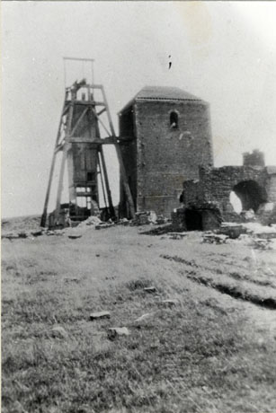 Photograph showing winding gear, a building and what appears to be the remains of a bridge or tunnel in the middle of a field; the photograph is described as The Colliery, Hutton Henry