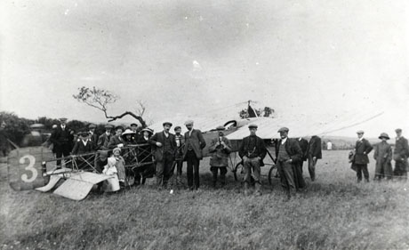 Photograph showing a field identified as Barn Field, Hutton Henry, in which is standing a small light aeroplane, the fuselage of which is constructed of open metalwork and the cockpit of which is open; the wings of the aeroplane have span of about twenty feet and the tail bears the number three; twenty three adults and two children are standing near the aeroplane