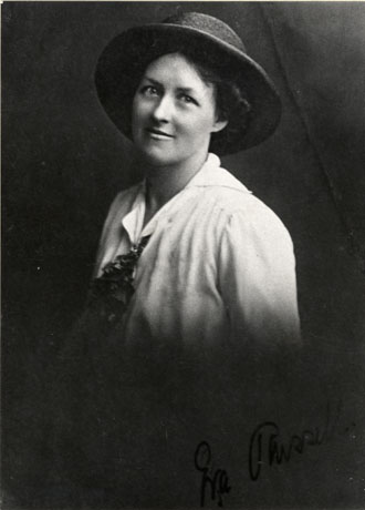 Photograph of the head and shoulders of a young woman wearing a straw hat, a blouse open at the neck and a loose tie; there is a signature on the photograph reading: Eva Russell