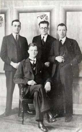 Photograph showing a man, wearing a suit, tie and wing collar, sitting with three young men in suits standing behind him; he has been identified as George Hobbs