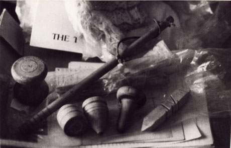 Photograph of a collection of objects of which, a whip and three tops can be seen at the front of the photograph; there is also a piece of wood with notches in it at the right and what looks like a bobbin at the left; it has been identified that the photograph includes Tippet and Diabolo as well as the whip and top