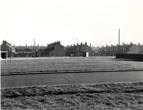 Photograph showing a road running across the picture with grass beyond it; beyond the grass are the ends and sides of five terraces and, in the distance, the rear of a terrace parallel to the road