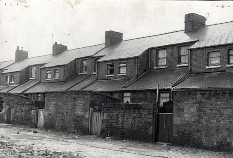 Photograph showing the rear of a terrace of houses, showing windows on the first floor, the roofs of the kitchens, the outhouses and the walls of the yards