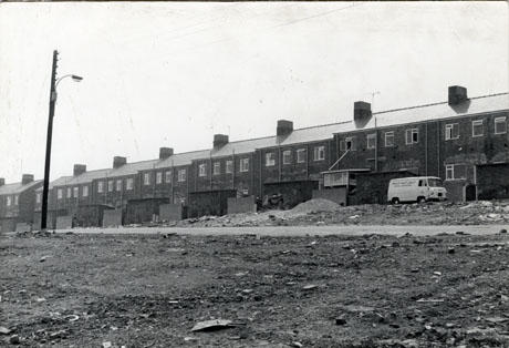 Photograph showing the rear of a newly-altered terrace of houses; the brick work round the new windows in the terrace indicates, possibly, that the terrace has been altered and modernised; a van can be seen outside one of the houses; there are a road and open ground strewn with rubble in the foreground of the picture, possibly indicating that houses have been demolished on the site