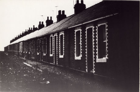 Photograph of the exterior of a terrace of single-storeyed houses, built of brick and with light coloured bricks outlining the windows and doors