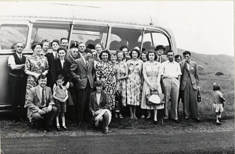 Photograph of a group of twenty five people standing outside a single-decker motor bus with a hillside behind it; two children are also present; the photograph has been identified as recording Drama Club Outing, Murton, 1950s
