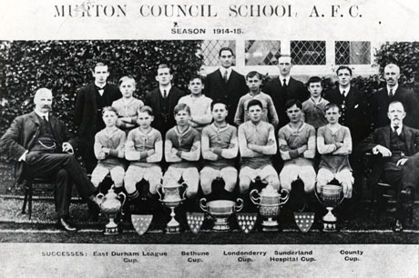 Photograph entitled Murton Council School Athletic Football Club Season 1914-15 and Successes : East Durham League Cup Bethune Cup Londonderry Cup Sunderland Hospital Cup County Cup, showing eleven members of the team in the team's strip, accompanied by eight men, posed in front of a building covered in ivy; in front of the group are nine trophies