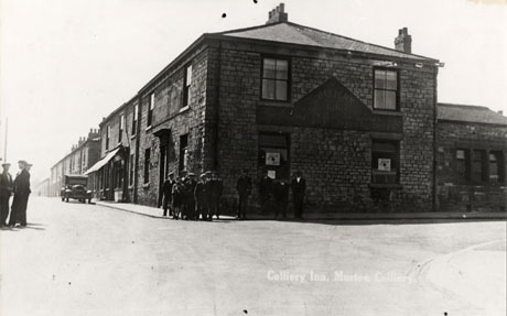 Postcard photograph entitled Colliery Inn, Murton Colliery, showing a plain stone building on the corner of two streets with the sign on the side of the building facing the camera two groups of approximately twelve men can be seen on the pavement and further three men can be seen in the road; a car is parked facing the camera beside a shop with an awning just beyond the inn