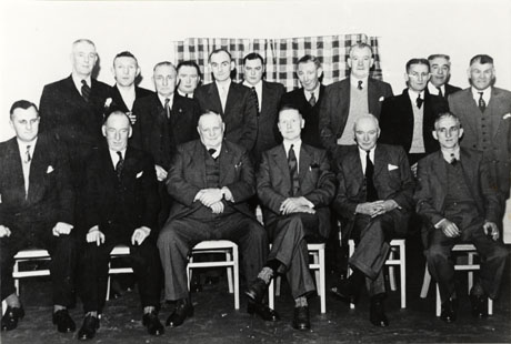 Photograph of seventeen middle-aged men posed against an interior wall; all of them are wearing suits and ties; they are identified as Victoria Club Committee, Murton Colliery; a number of the men may be the same as those on murt0018