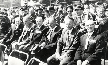 Photograph of rows of spectators at The Presentation For Mr. McNally (awarded Victoria Cross) in Murton; in the foreground, running from left to right, is a row of six men in civilian dress wearing medals; behind them is a row of guests, which include three high-ranking members of the armed forces, two men in suits, and three women of the same social class; beyond them are two rows of individuals, who cannot be distinguished in any detail