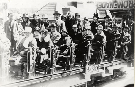 Photograph of approximately twenty-five people sitting on an open railway train with the number 360 at its front; people can be seen sitting on benches and the remainder are standing behind them; the word promenade can be seen behind the train, as can the roof of an unidentified building; the photograph has been identified as Outing at Blackpool, Miners' Families, Murton, 1930s