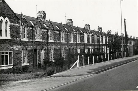 Photograph of the facade of a terrace of houses with bands of lighter coloured brick across at three levels; the windows of the houses are divided into two and have pointed tops; they have been identified as possibly Darcy Place;approximately twenty six houses can be seen