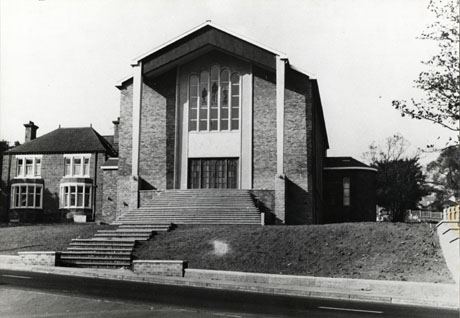 Photograph of the exterior the west end of the new Roman Catholic Church at Murton; the church has a long flight of steps and is built of brick; it has a large stained glass window at the west end; beyond the church a pair of semi-detached houses can be seen
