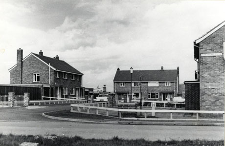 Photograph of a cul-de-sac of four semi-detached houses; two can be seen from the side and front and two from the front; a road leads past another two houses which cannot be seen other than by part of their end wall; the hoses are typical semi-detached houses of the 1970s with two large windows on the first floor and one large picture window in the ground floor; the front door has a porch consisting of a canopy supported by poles; the houses have been identified as Hawthorn Close, Murton