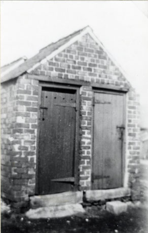 Photograph of the exterior of outside lavatories showing a small brick hut with two wooden doors in the front; they have been identified as being in Murton Colliery