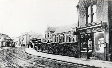 Postcard photograph entitled Church Street, Murton, showing a road running away from the camera to the right; on the right of the road are the windows of the shop of Platts, Newsagent, followed by the facade of a large building behind a wall; at the end of the street is a large public house; on the left of the street are only a few indistinct buildings at the end of the road can be seen; approximately five indistinct figures can be seen on the pavement