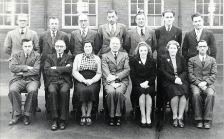 Photograph of eleven men and three women posed in the playground of school with the exterior of the school behind them; the men are all wearing suits and ties; two of the women are also wearing suits and the third is wearing a skirt and blouse; they have been identified as Murton Senior Boys' Staff, 1949