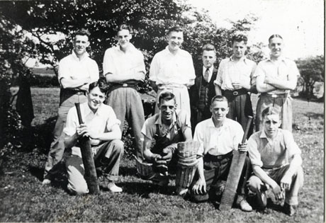 Photograph of ten young men posed against trees and on grass; the four on the front row are kneeling, one of whom is wearing cricket pads and two of whom are holding bats; they have been identified as members of Murton Bakery Cricket Team