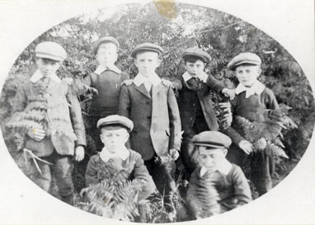 Photograph of seven boys, aged approximately ten years, wearing suits, caps and Eton collars, and photographed in front of trees and bracken; they have been described as Sunday School Class, 1912