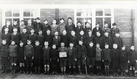 Photograph of forty four boys, aged approximately ten years, posed in front of a brick building; a boy on the front row is standing with crutches as he has only one leg; another boy on the front row is holding a notice on which the numbers 1924 and 6 can be seen; they have been identified as Class 6, Murton School, 1924