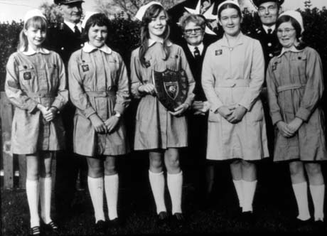 Photograph of five girls, aged approximately twelve years, dressed in uniform, standing in a row; behind them are two middle-aged men and a middle-aged woman in the uniform of the St. John Ambulance Brigade; one of the girls is holding a shield; they have been identified as cadets of the St. John Ambulance Brigade and the middle aged man and woman as Mr. and Mrs. S. Cummings of Horden