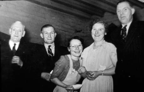 Photograph showing three men and two women standing in a group and laughing; one woman has her hand through the arm of the other and is holding a piece of paper; the photograph has been described as Have A Go, Murton