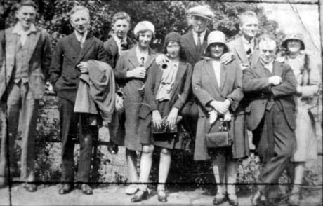 Photograph showing six men in suits and five women in overcoats and suits, standing in front of a garden wall with trees behind it; they have been identified as employees of a bakery in Murton on its annual outing