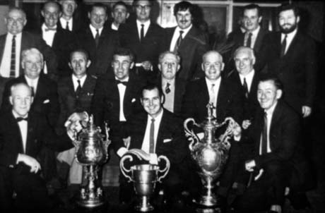 Photograph of the head and shoulders of eighteen men, in suits and dinner jackets, in three rows, with three trophy cups in front of them; they have been described as Officials' Club Snooker Team - Top Division, Murton; the officials are presumably those of the colliery in Murton