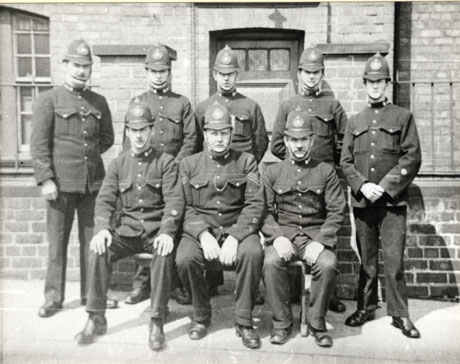 Photograph of seven police constables and a police sergeant, all in uniform, posed in front of a brick building with a door and a window in the picture; they have been identified as being in Murton