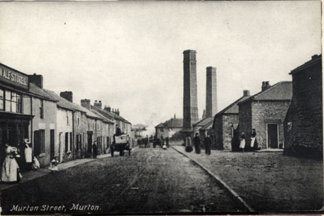 Postcard photograph entitled Murton Street, Murton, showing a road running away from the camera with terraced houses on the left and the ends of blocks of houses and two tall chimneys on the right; part of the front of a shop with the words ..n Ale Stores can be seen on the left; carts are moving up and down the road and figures are standing on the pavements
