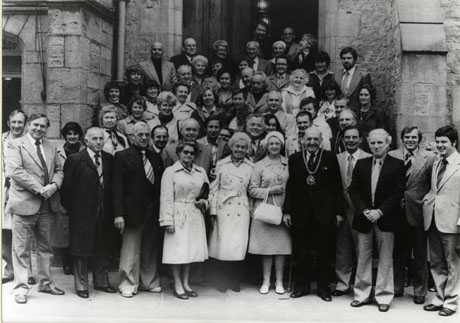 Photograph of a group of approximately sixty middle-aged people posed in the doorway of what appears to be a church; a man wearing a chain of office is standing on the front row; the photograph has been identified as Baesweiller Visit, Durham, 1978