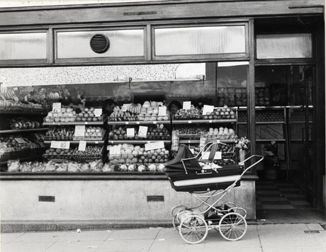 Photograph of the exterior of a fruit shop; the contents of the shop window, shelves of fruit, can be seen in detail and shelves of fruit can be seen indistinctly inside the shop; outside the shop, a perambulator can be seen; the shop has been identified as being in Peterlee