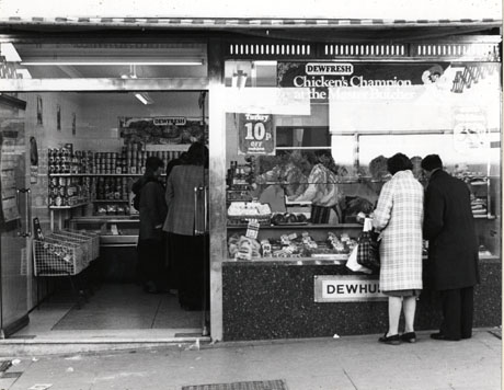 Photograph of the exterior, and part of the interior, of Dewhurst's Butcher's shop; tinned goods can be seen on shelves in the shop, as can the rear of customers and the profile of a man serving; the meat in the shop window and the rear of two customers looking in the window can also be seen; the shop has been identified as being in Peterlee
