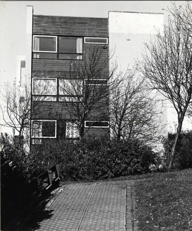 Photograph of the exterior of a three-storey block of flats; the building is faced with wood and brick and has a flat roof; a path leads from the camera to the building and there are trees and grass in front of it; it has been identified as View From Manor Way, Peterlee