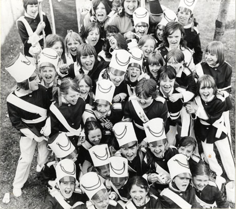 Photograph of approximately forty girls of between twelve and fifteen years in a uniform of tunic, sash, helmet and light-coloured trousers, grouped together and looking up at the camera; they have been identified as Peterlee Emeralds Jazz Band