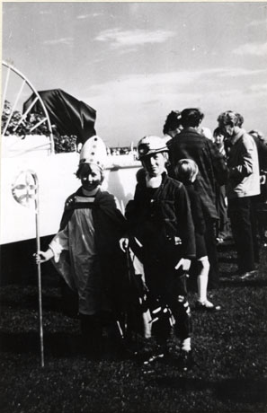 Photograph of a child dressed as a bishop and a child dressed as a miner; behind the children four adults and one child can be seen talking to each other; the photograph has been identified as 25th Jubilee Carnival of Peterlee